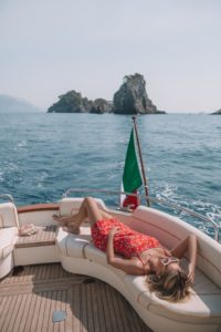A model sunbathing on the back of a gozzo boat with sea and an island