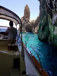 A gozzo boat moving among rocks in a blue sea