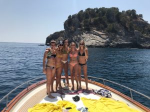 A group of girls standing on the front of the boat with an island on the sea
